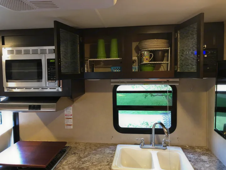 Well-equipped RV rental kitchen featuring a microwave, sink, stovetop, and overhead cabinets with dinnerware storage.. Dutchmen Kodiak 2016