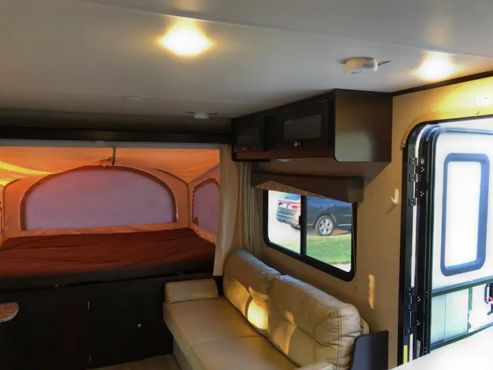 RV rental interior showing a comfortable bed in a pop-out, sofa, and cabinets.. Dutchmen Kodiak 2016