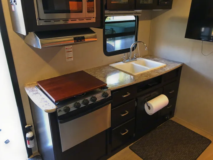 Well-equipped rv rental kitchen: stove, sink, microwave, storage, and small window. Perfect for road trips.. Dutchmen Kodiak 2016