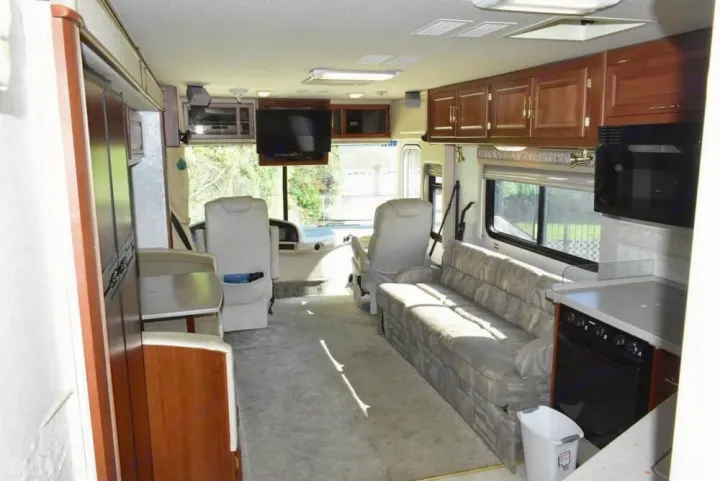 RV rental interior: living area with couch, full kitchen, and driver's cockpit. Features overhead cabinets, appliances, and plush seating.. Fleetwood Expedition 2003