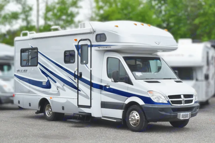 A white and silver Class C rv rental with blue stripes, built on a Dodge Sprinter chassis, parked on asphalt outdoors.. Fleetwood Pulse 2009