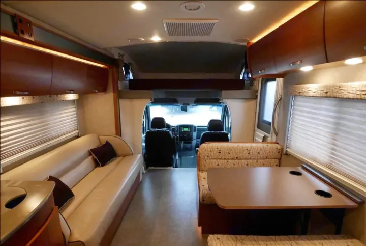 Bright rv rental interior featuring a comfortable sofa, dinette, and overhead bunk, leading to the cockpit.. Fleetwood Pulse 2009