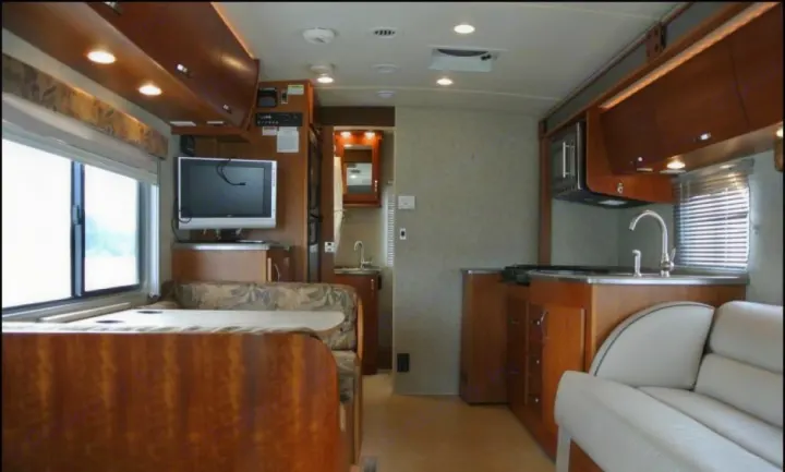 This rv rental features a cozy interior with a dinette, kitchen, TV, and comfortable sofa.. Fleetwood Pulse 2009