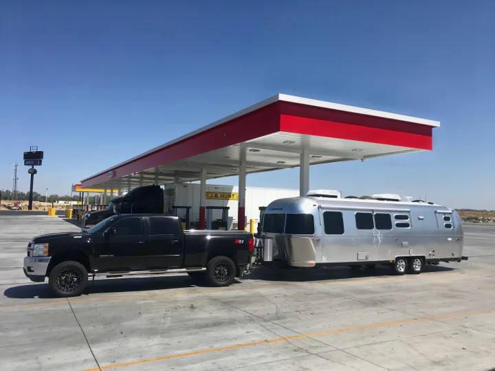 Black pickup towing a shiny Airstream RV at a sunny gas station.. Airstream Flying Cloud 2020