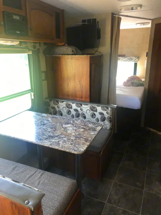 Inside an RV rental: a compact living space with a dinette, table, overhead storage, and a glimpse of the bedroom for cozy travels.. Keystone Hideout 2016