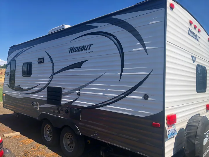 A white and gray Hideout by Keystone travel trailer, ready for an RV rental adventure, parked on a sunny day.. Keystone Hideout 2016