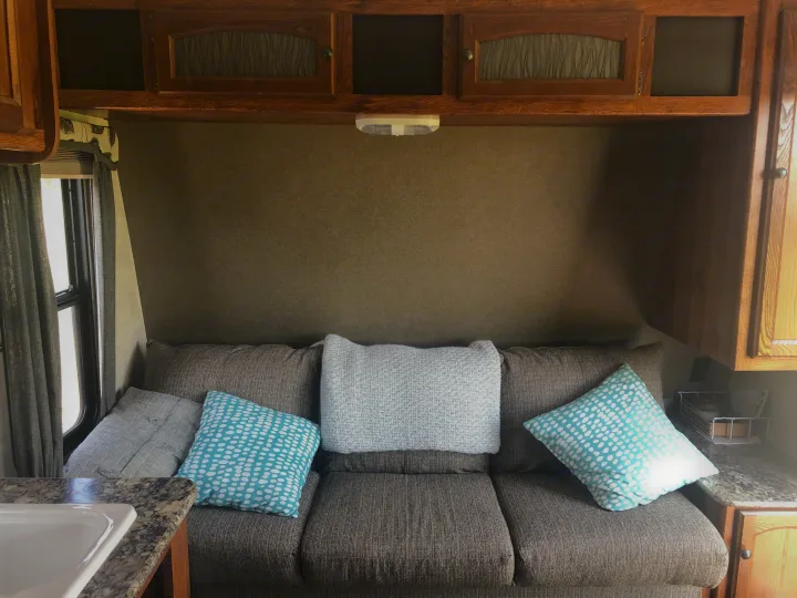 Comfortable brown couch with blue and white patterned pillows inside an RV rental, featuring wood cabinets and a window.. Keystone Hideout 2016
