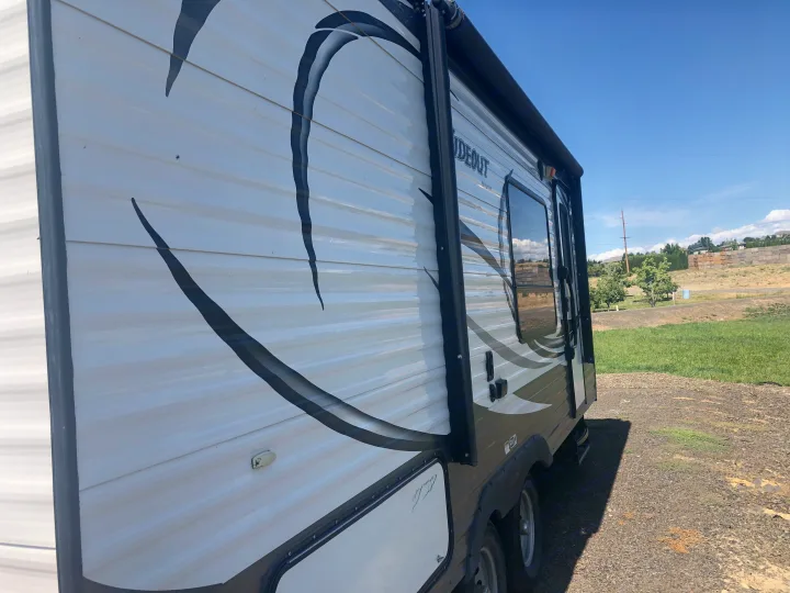 This clean white RV rental, with black and grey graphics, is perfectly parked on gravel under a clear blue sky.. Keystone Hideout 2016