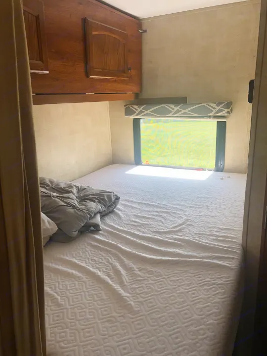RV rental bedroom with bed, cabinets, and window. Sunlight brightens the compact sleeping area.. Keystone Hideout 2016