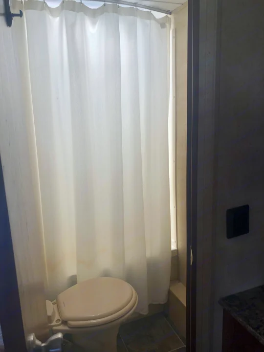 Compact RV rental bathroom featuring a toilet and white shower curtain.. Keystone Hideout 2016