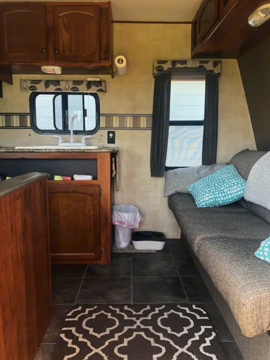 Inside an RV rental: kitchen with sink, wood cabinets, and cozy living area with sofa and patterned rug.. Keystone Hideout 2016
