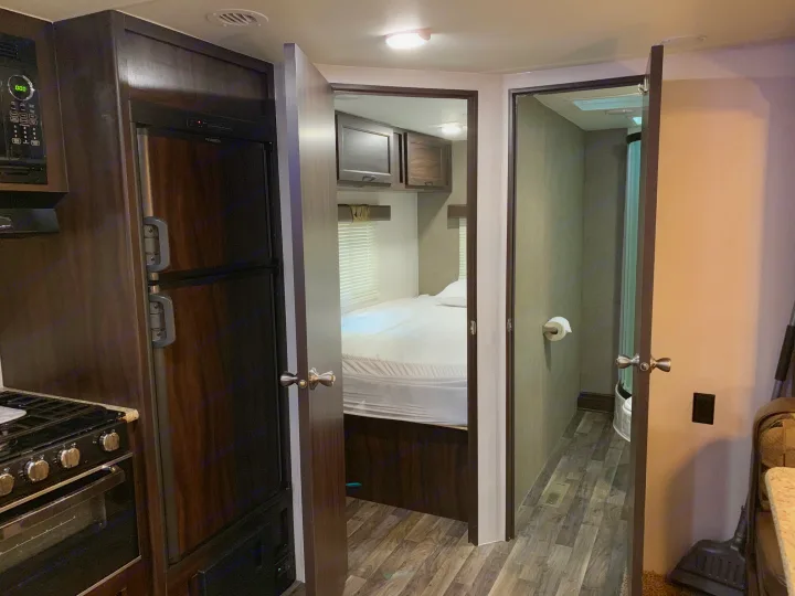 RV rental interior featuring a compact kitchen (fridge, microwave, stove), open to a bedroom and bathroom.. Pacific Coachworks Tango 2020