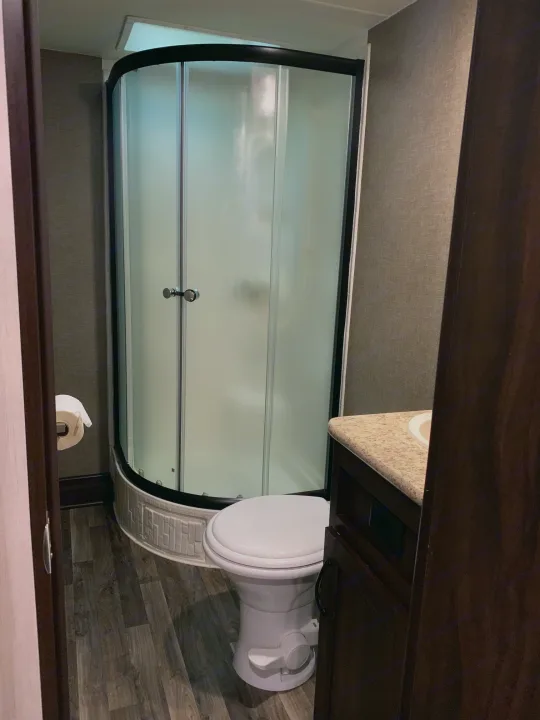 RV rental bathroom featuring a curved shower, toilet, vanity, and wood-look flooring, showing its compact layout.. Pacific Coachworks Tango 2020