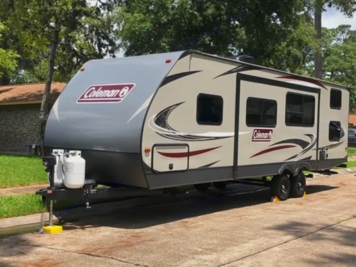 A light-colored Coleman travel trailer, parked on pavement with propane tanks upfront. Ideal for an RV rental vacation.. Dutchmen Coleman 2855BH 2019