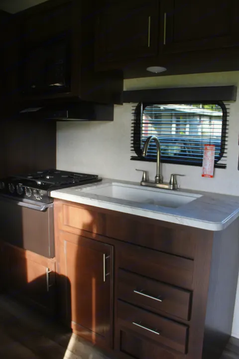 Spacious RV rental kitchen with dark wood cabinets, stove, microwave, and sink, ready for adventure.. Jayco Jay Flight SLX 2019