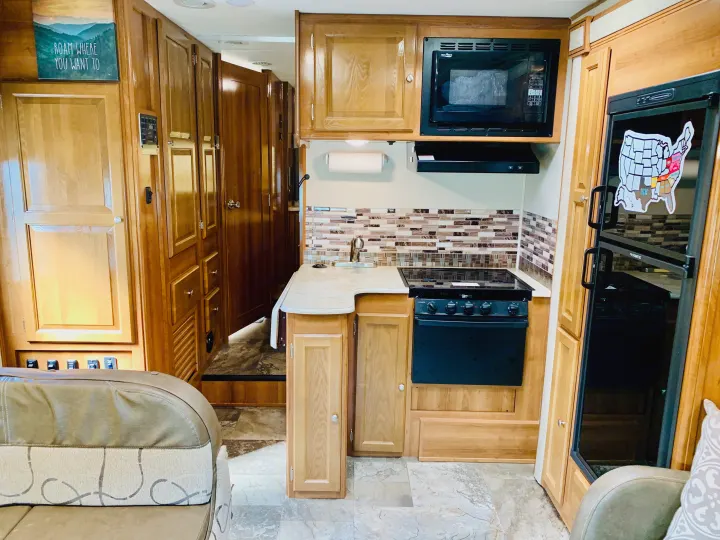 RV rental interior showcasing a full kitchen with microwave, stove, fridge, and ample wood cabinetry; comfy seating visible.. Coachmen Leprechaun 2018