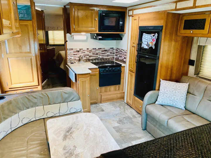 This rv rental features a compact interior with a full kitchen, living space, and bedroom beyond.. Coachmen Leprechaun 2018