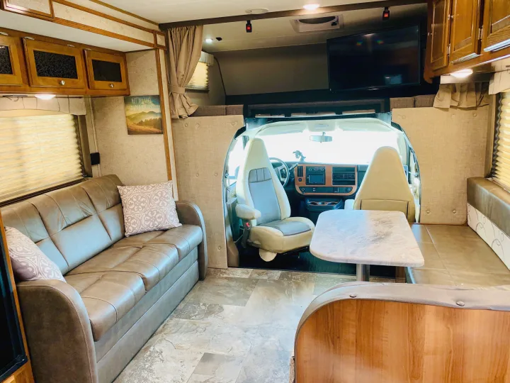 Bright RV rental interior featuring a comfortable sofa, dining area, and spacious driver's compartment.. Coachmen Leprechaun 2018