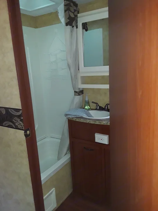 Peek into bathroom, medicine cabinet behind mirror, mesh under sink for laundry, shower tub, ceramic toilet behind door. Keystone Outback BH312 2011