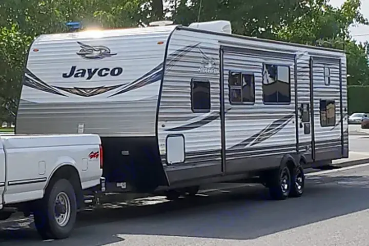 A large Jayco travel trailer, white with gray stripes, is hitched to a white pickup truck. A great option for an RV rental.. Jayco Jay Flight 2019