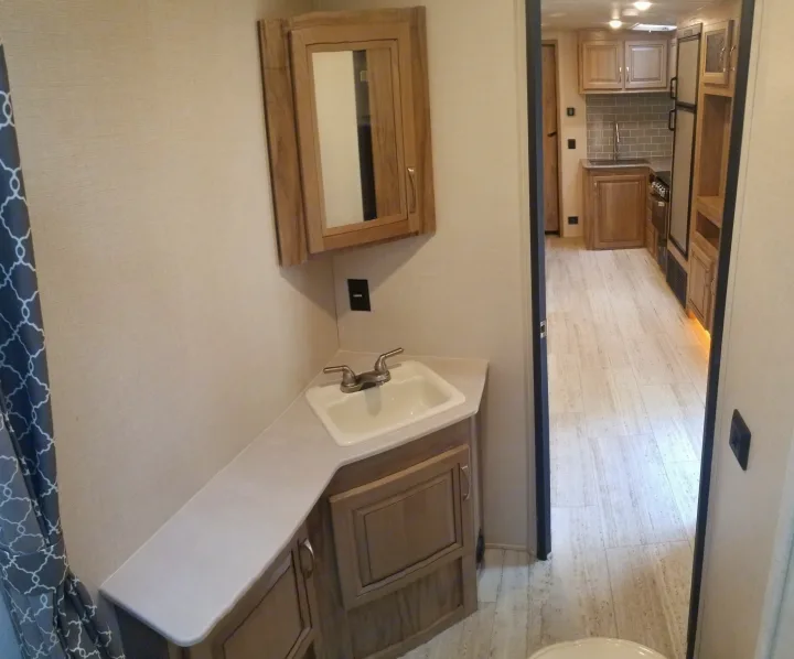 Modern RV rental interior: bathroom vanity with sink and mirror, opening to a well-equipped kitchen with appliances and cabinets.. Palomino Solaire Ultra Lite 268BHSK 2020