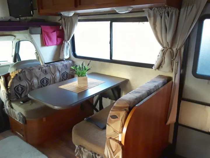 Cozy RV rental dinette features patterned booth seating, a table with a plant, and bright windows, offering a comfortable space.. Coachmen Freelander 2011