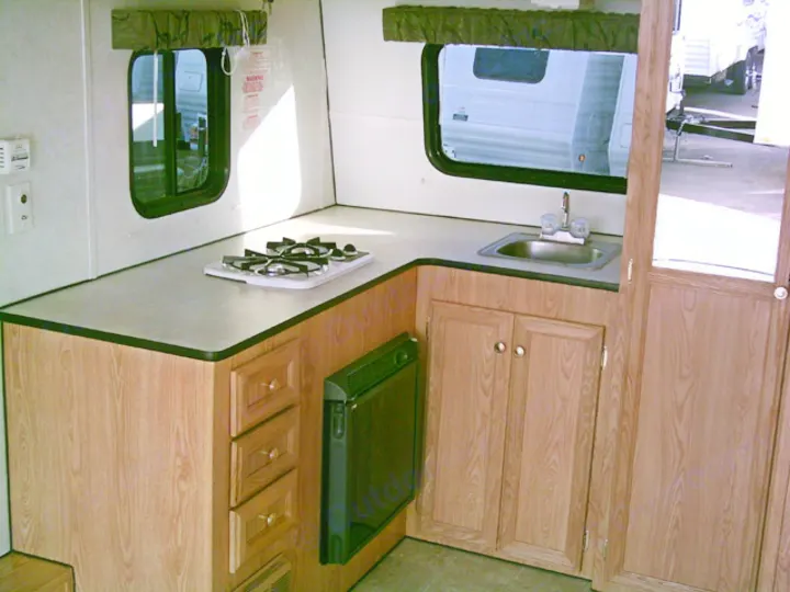 RV rental kitchen: Countertop with gas stove, sink, wood cabinets, and window in a compact space.. Carson Trailer Toy Hauler 2007