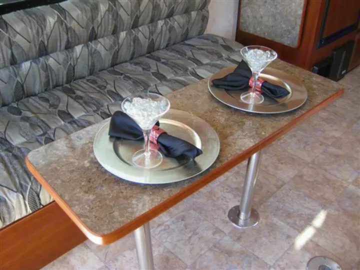RV rental dining area: A table set for two with martini glasses, plates, and napkins, next to patterned bench seating.. Carson Trailer Toy Hauler 2007