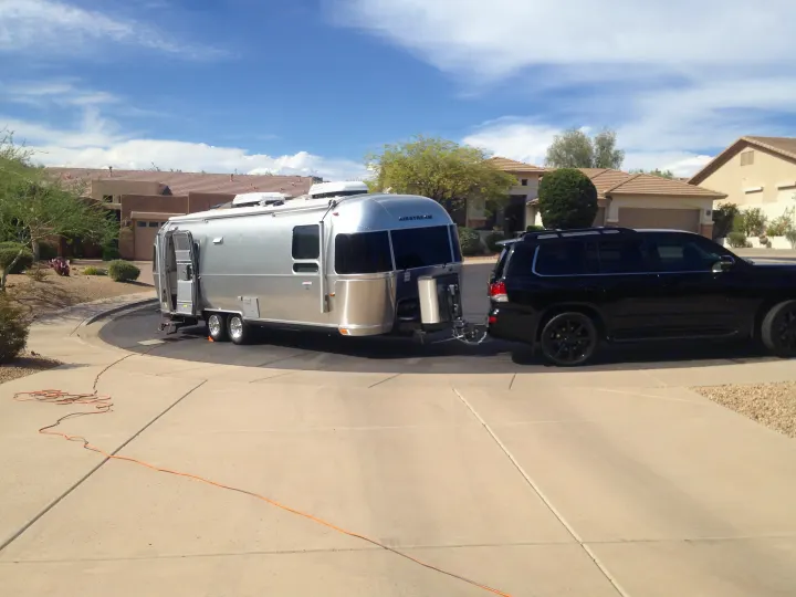 Silver Airstream rv rental and black SUV on a suburban driveway. Perfect for your next road trip adventure.. Airstream International 2015