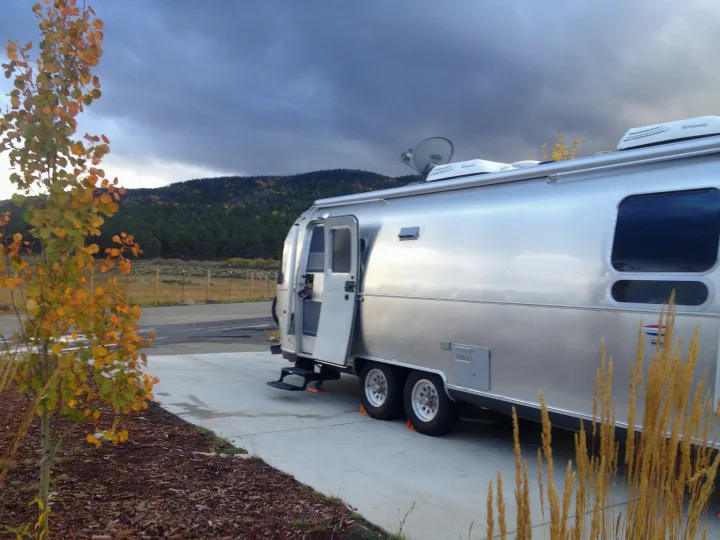 A silver travel trailer with open door, possibly an RV rental, parked on pavement. Dry grass foreground, mountains beyond.. Airstream International 2015