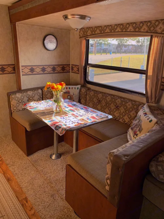Relax in this RV rental's inviting dinette! Features a U-shaped bench, table with flowers, & scenic window.. Keystone Passport 2014