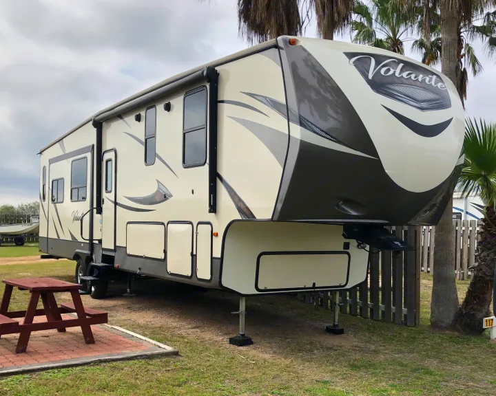 Spacious Volante fifth-wheel RV parked at a scenic site with a picnic table and palm trees, ideal for an RV rental getaway.. Keystone Volante 3801MD 2018