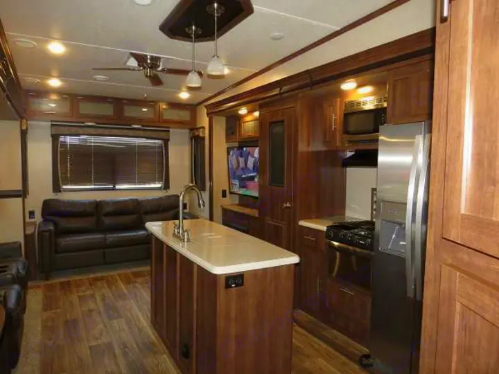 Discover this inviting RV rental interior with a fully equipped kitchen, central island, and comfortable living area sofa.. Keystone Volante 3801MD 2018