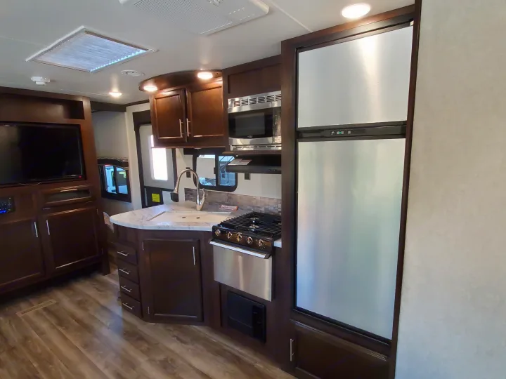 Inside this RV rental, a well-equipped kitchen boasts stainless appliances, sink, and dark wood cabinetry, plus a TV area.. Jayco Jay Flight 2019