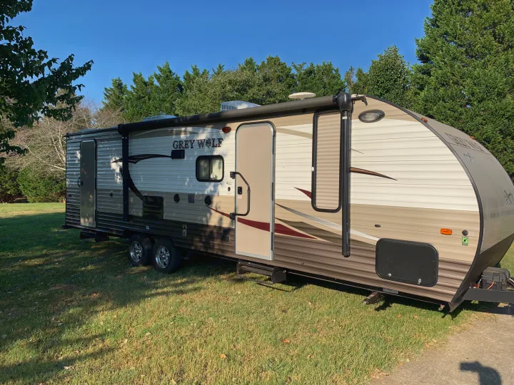 Grey Wolf travel trailer parked on grass, ideal for an RV rental adventure under a clear sky, surrounded by trees.. Forest River Cherokee Grey Wolf 2016