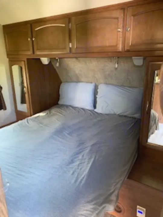 This cozy RV rental bedroom features a queen bed, built-in storage, and reading lights, perfect for your travel accommodation.. Coachmen Freedom Express - Liberty Edition 2017