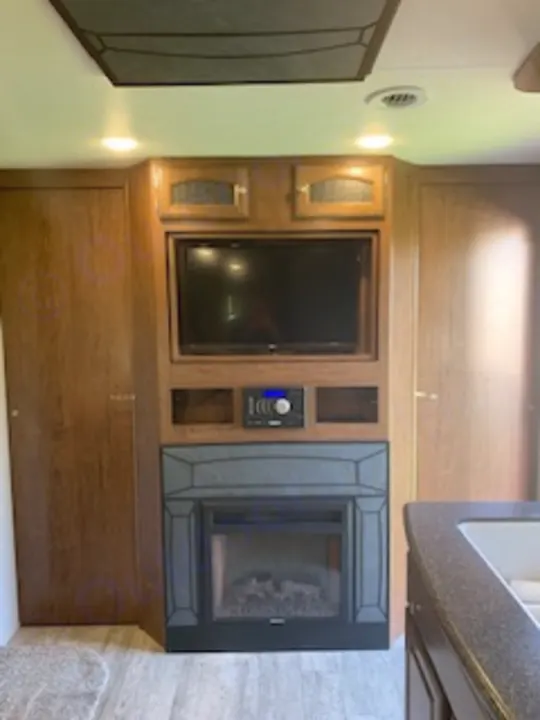 Cozy RV rental living space featuring a built-in TV, stereo, and electric fireplace within warm wood cabinetry.. Coachmen Freedom Express - Liberty Edition 2017