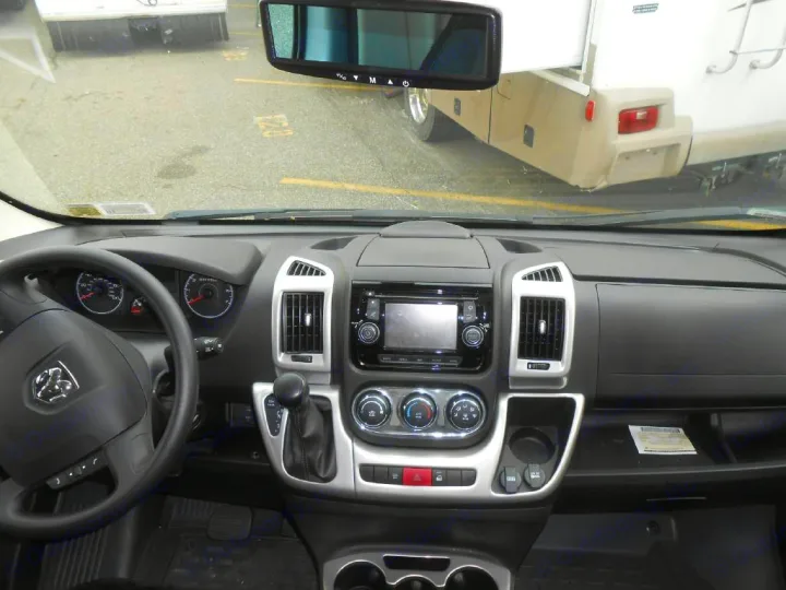 RV rental interior: driver's view of the dashboard, steering wheel, and console. Another RV is seen through the windshield.. Winnebago Trend 2016