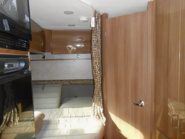 Cozy RV rental interior with a compact sleeping area, microwave, and wood cabinets, perfect for adventures.. Winnebago Trend 2016