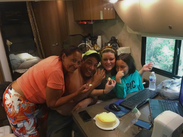 A joyful family of four shares cake and uses laptops inside a cozy RV rental, enjoying their time together.. Winnebago Trend 2016