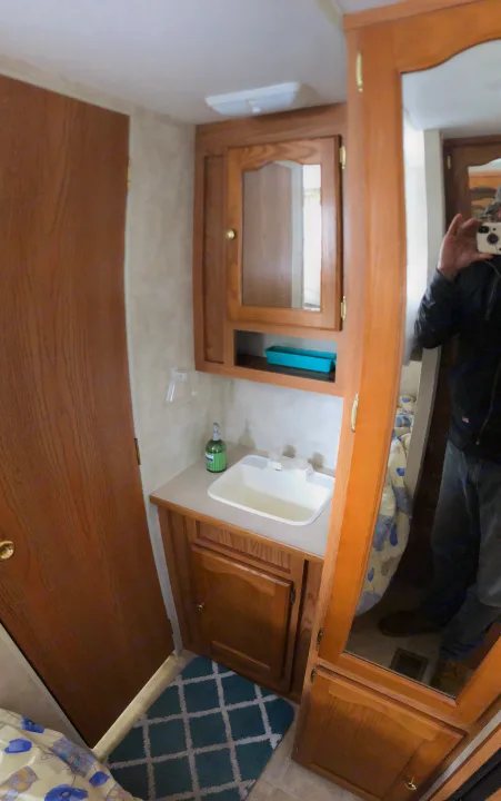 Tour an RV rental bathroom with a sink, mirror, and oak cabinets. Includes a patterned rug & green bottle.. Keystone Springdale 2004