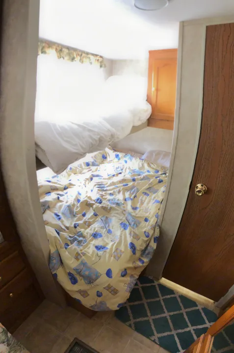 An inviting RV rental bedroom featuring a yellow and blue floral comforter, a blue patterned rug, and wooden cabinetry.. Keystone Springdale 2004
