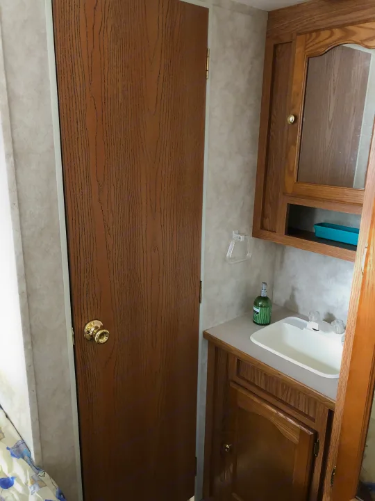RV rental: a wooden door with brass knob, compact sink, and oak cabinets define this functional interior space.. Keystone Springdale 2004