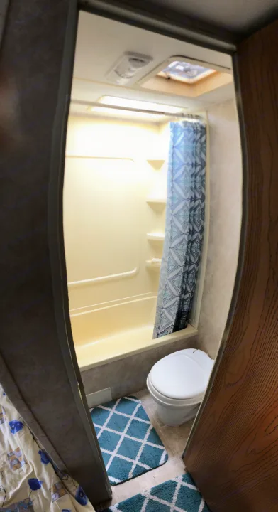 Compact RV rental bathroom showing a white toilet, blue patterned floor mats, and a shower area with a curtain.. Keystone Springdale 2004