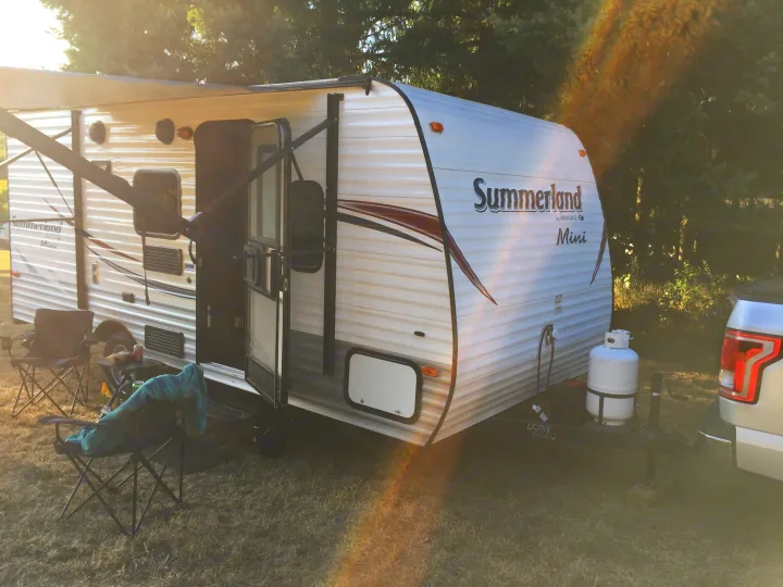 White Summerland Mini RV rental with extended awning, parked at a sunny campsite with chairs & truck.. Keystone RV Summerland Mini 2015