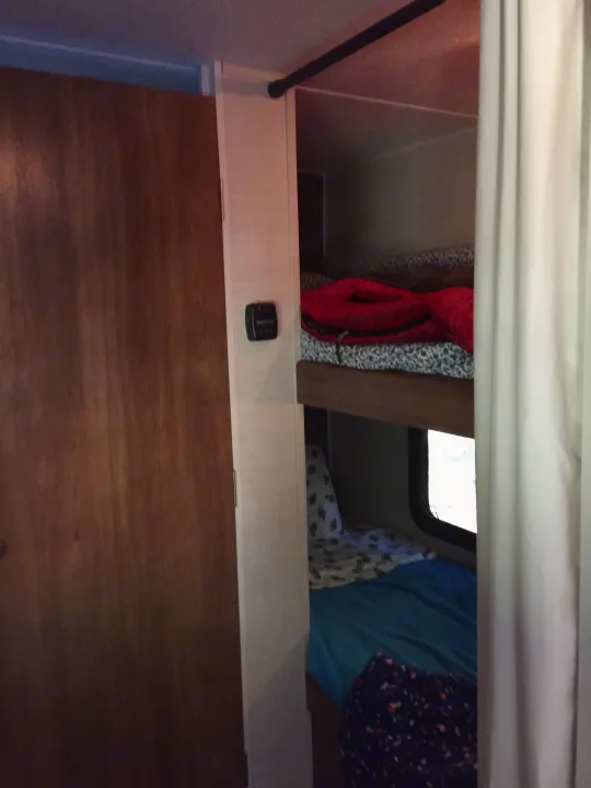 **RV rental**: Inside, a compact bunk bed area features blue bedding, clothing, a window, and a small device.. Keystone RV Summerland Mini 2015