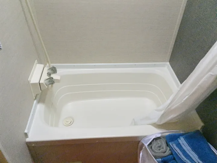 This compact white bathtub and shower unit in an RV rental bathroom features a curtain and essential amenities, including towels.. Keystone RV Summerland Mini 2015
