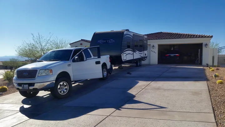 White truck hitched to an Aspen Trail RV rental, parked in a sunny driveway, ready for a trip.. Dutchmen Aspen Trail 2018