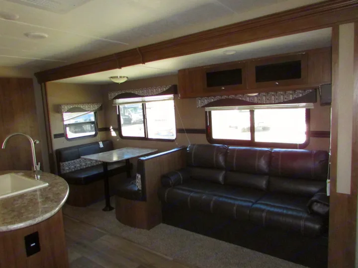 RV rental interior: A functional living space featuring a kitchen sink, dinette with booth seating, and a comfortable dark sofa.. Dutchmen Aspen Trail 2018