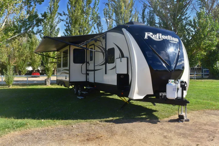 A cream and black "Reflection" travel trailer RV rental parked on sunny grass with its awning out.. Grand Design Reflection 2019
